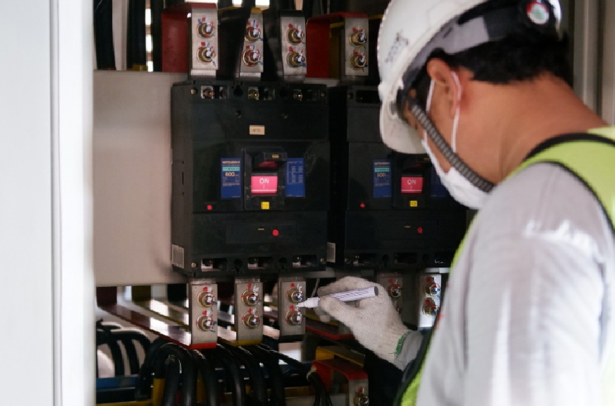 Worker inspecting and labeling industrial-grade circuit breakers in an electrical panel