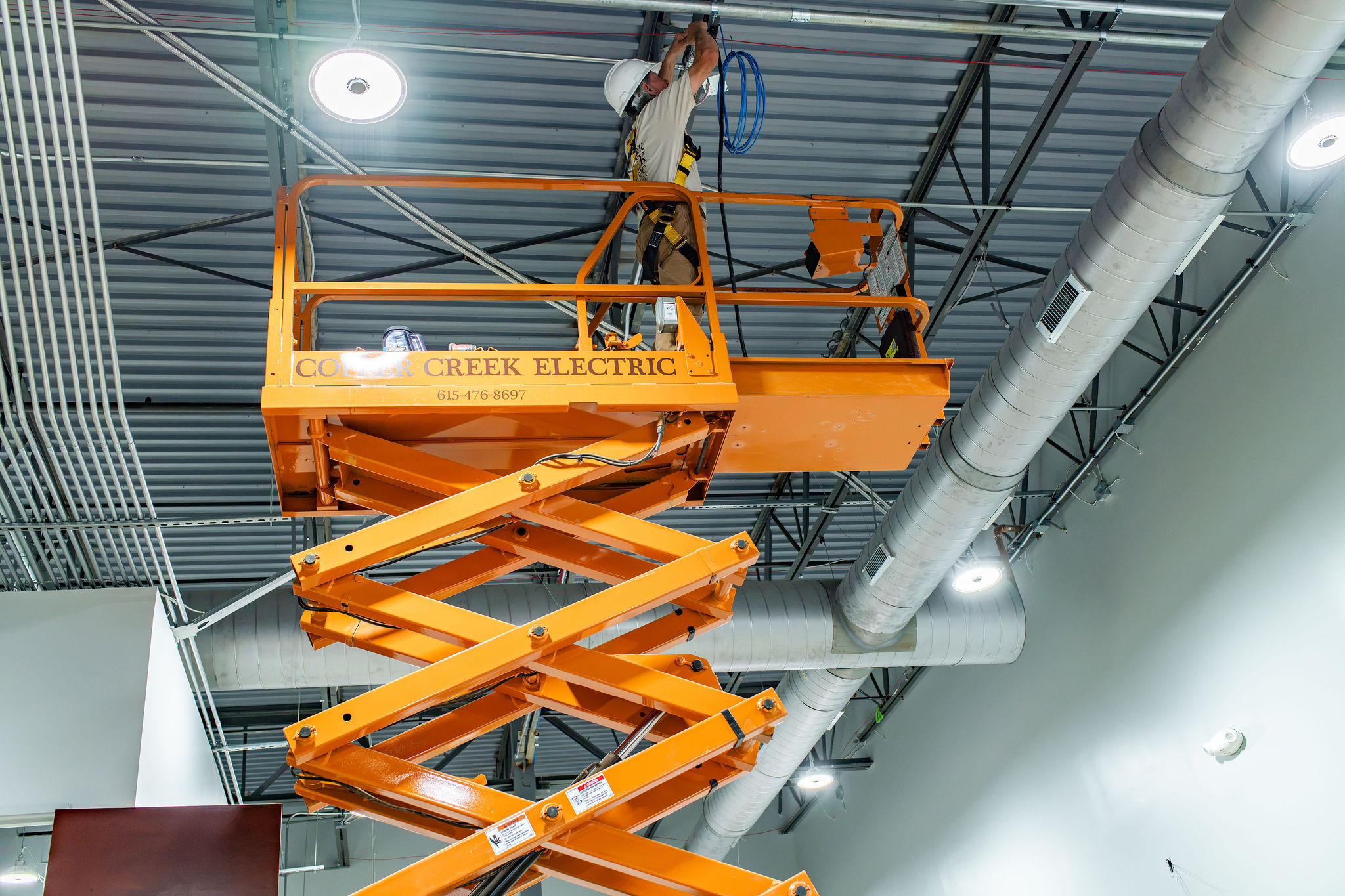Copper Creek Electric - Industrial Electrical Services - technician on a scissor lift installing high-bay warehouse lighting